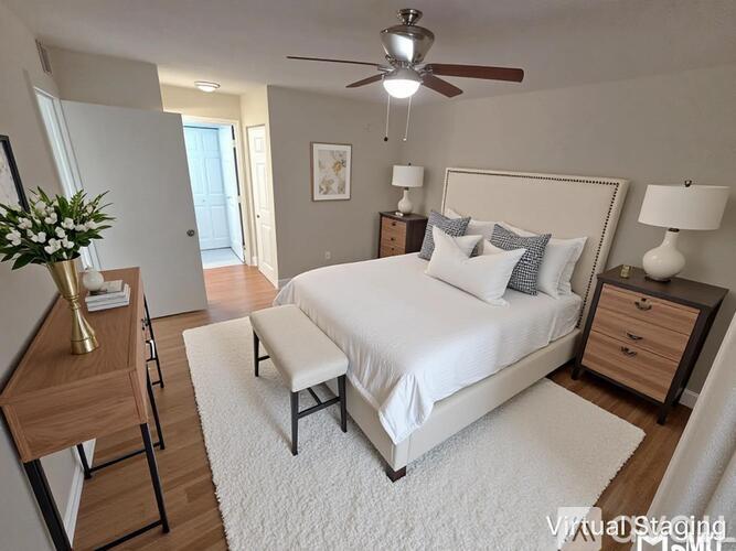 A bedroom with a large bed, a ceiling fan, and a nightstand with a lamp.
