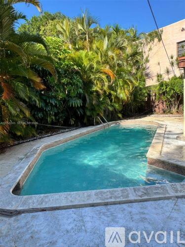 A small pool surrounded by greenery and a building in the background.