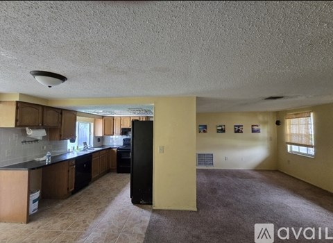 A spacious living room with a kitchen area and a refrigerator.