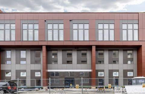 A large building with a red and grey facade and a car parked in front.