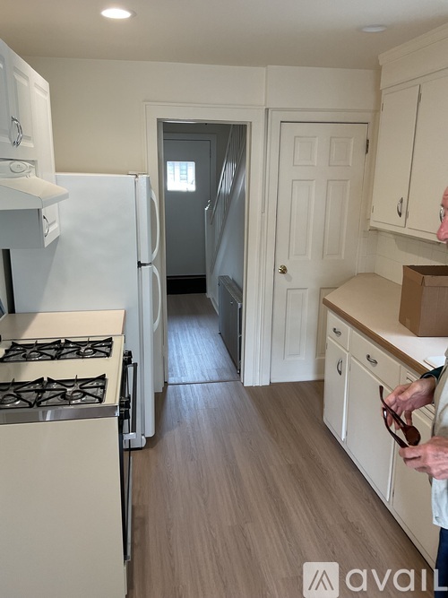 A man is holding a pair of sunglasses in a kitchen with white cabinets and a stove.