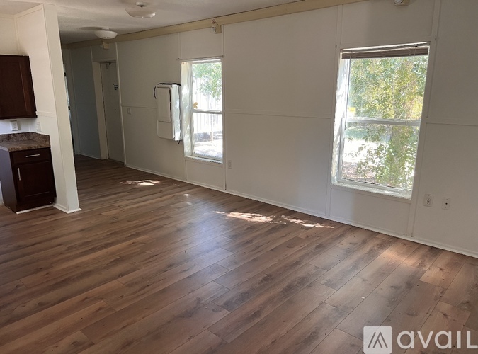A room with wooden flooring and a window showing trees outside.