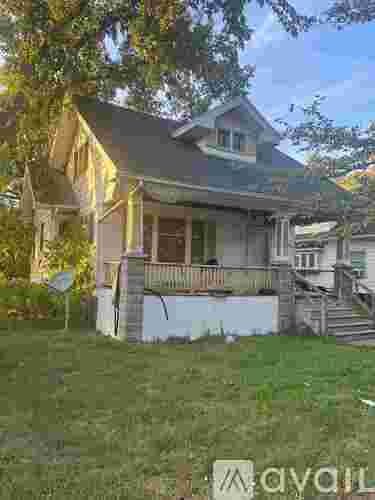 A house with a porch and a tree in front of it.