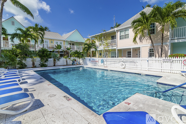 A pool surrounded by palm trees and a white fence.