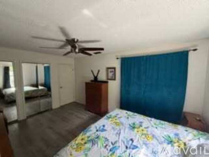 A bedroom with a bed, a ceiling fan, and a dresser with a mirror.
