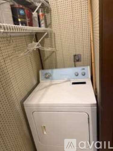 A white washing machine is tucked into a small space under a shelf.