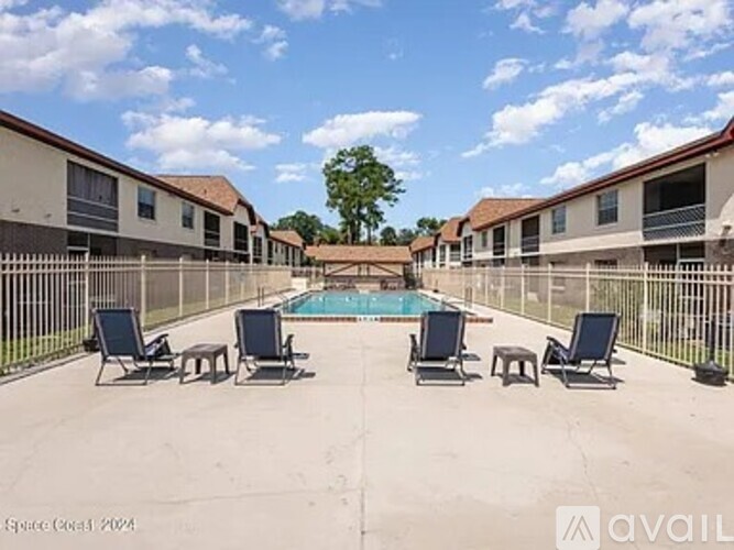 A pool surrounded by lounge chairs in a sunny courtyard.