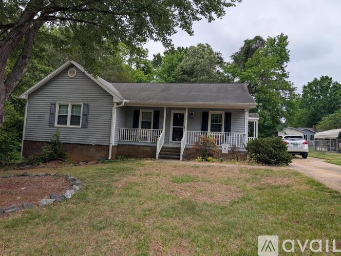 A house with a grey roof and a porch is surrounded by trees and grass.