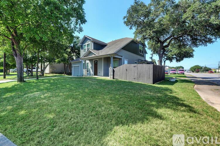 A house with a grey roof and a white garage door is surrounded by a green lawn and trees.