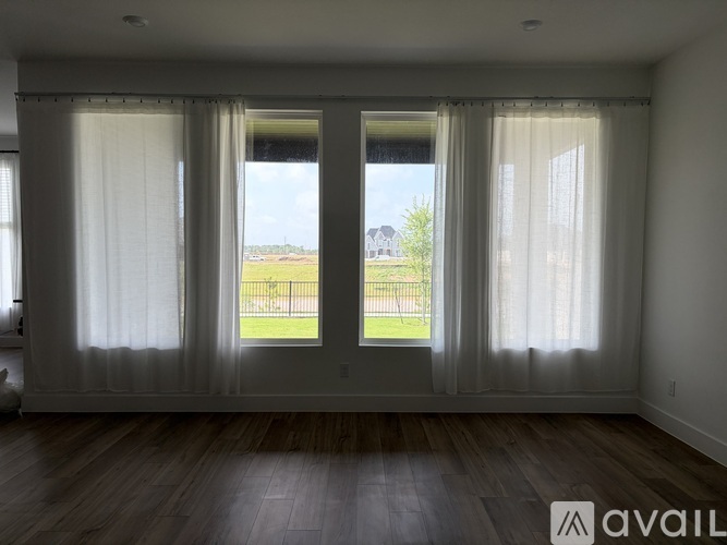 A room with a view of a fence and a house through the windows.