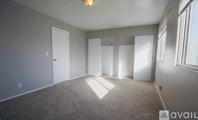 A spacious room with a carpeted floor and a large window on the right side.