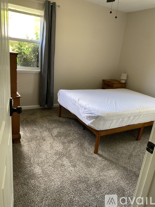 A bedroom with a bed, nightstand, and window with curtains.