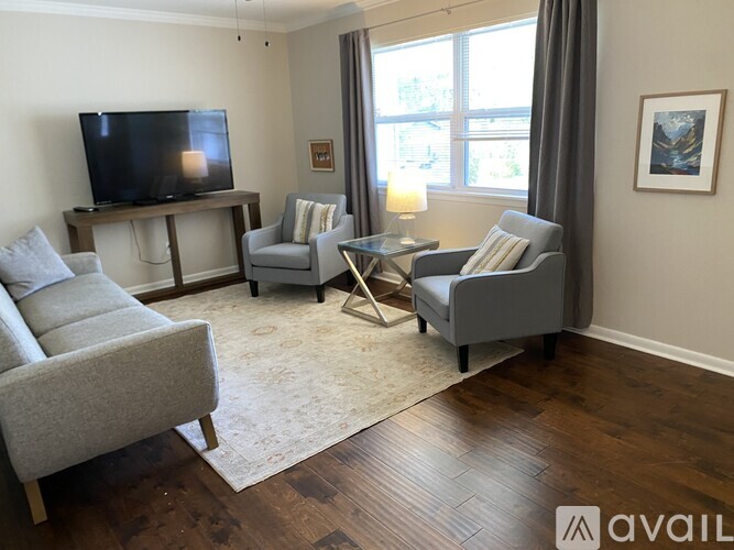 A living room with a grey couch, a chair, a coffee table, and a television on a wooden stand.