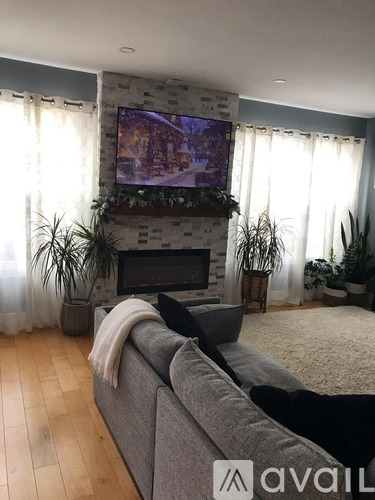 A living room with a grey couch and a television mounted above a fireplace.