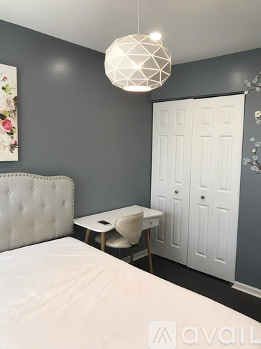 A bedroom with a white bed and a white desk with a chair.