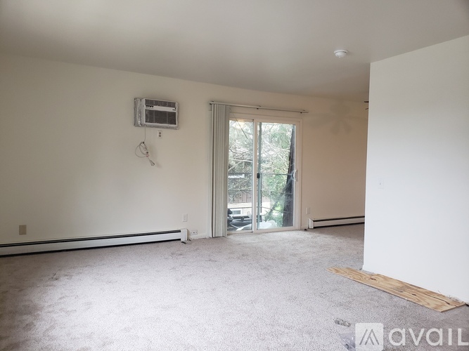 A room with a carpeted floor, a window with a sliding door, and a wall-mounted air conditioner unit.