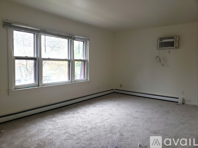 A room with a carpeted floor, a window, and a wall-mounted air conditioner unit.
