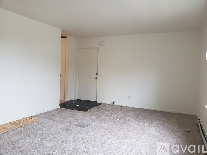 A room with a carpeted floor and a door is available for rent.