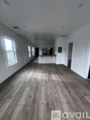 A spacious room with wooden flooring and white walls.
