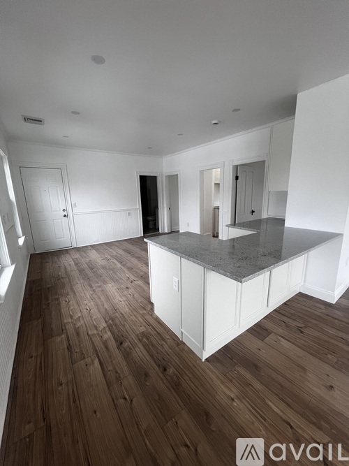 A spacious kitchen with wooden floors and white cabinetry.