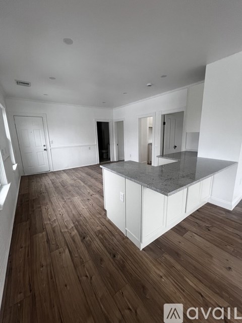 A spacious kitchen with wooden floors and white cabinetry.