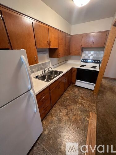 A kitchen with a white refrigerator, brown cabinets, and a tiled floor.
