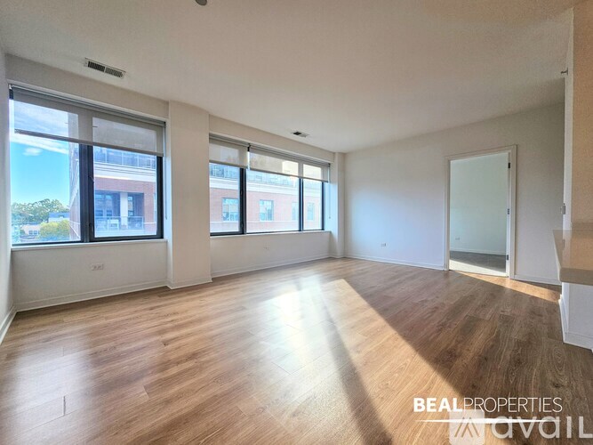 A spacious room with wooden flooring and large windows.