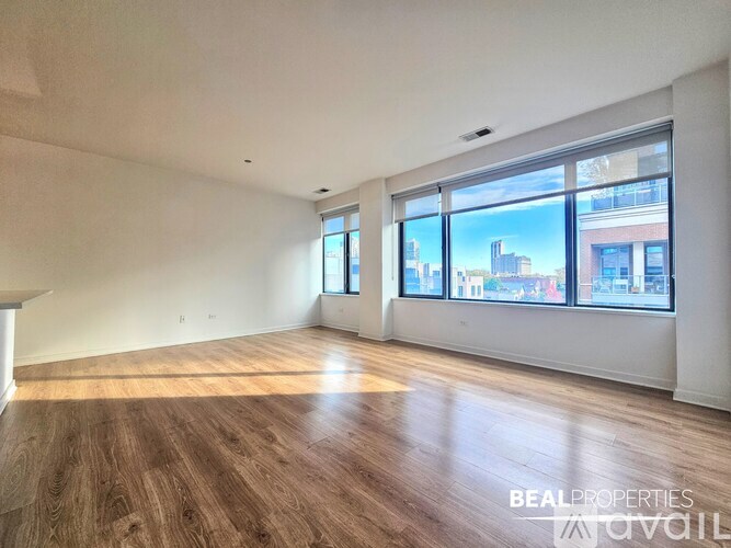 A spacious room with wooden flooring and large windows overlooking a cityscape.