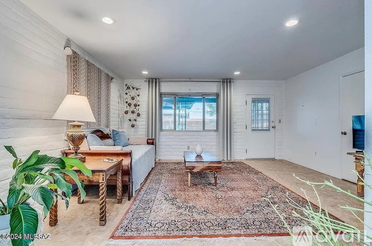 A well-lit room with a large rug, a wooden table, and a sofa.