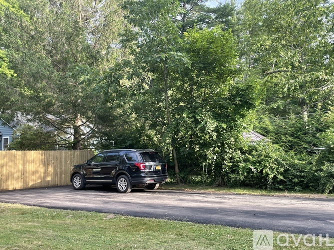A black SUV is parked on a driveway in front of a wooden fence and green trees.