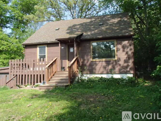 A house with a brown siding and a brown deck is surrounded by greenery.