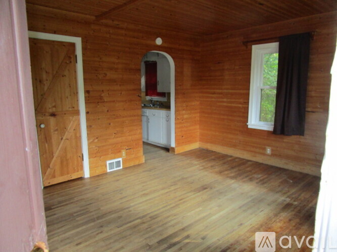 A room with wooden walls and floor and a white refrigerator.