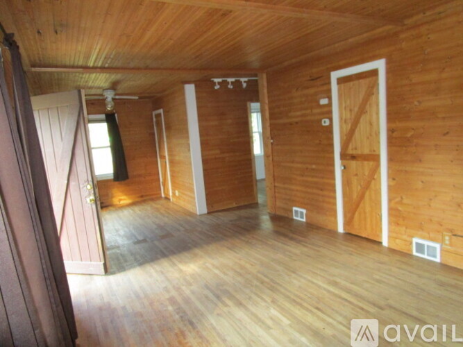 A room with wooden walls and floors, a ceiling fan, and a door on the right.