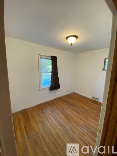 A room with wooden flooring and a window with a black curtain.