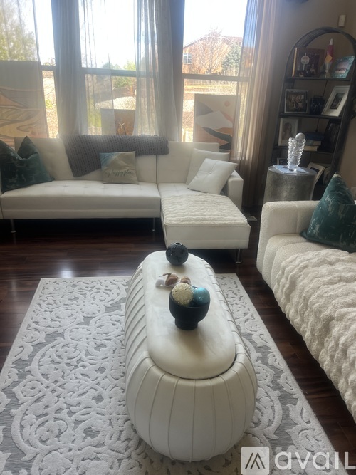 A living room with a white couch and a white ottoman with a decorative item on top.