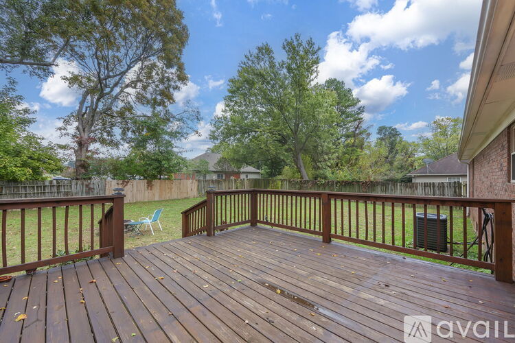 A wooden deck with a railing and a chair is surrounded by a grassy area and trees.