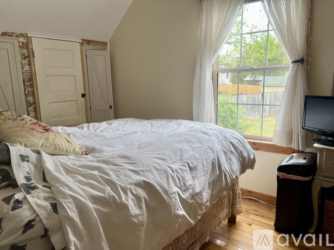 A bedroom with a bed, a window with curtains, and a television.