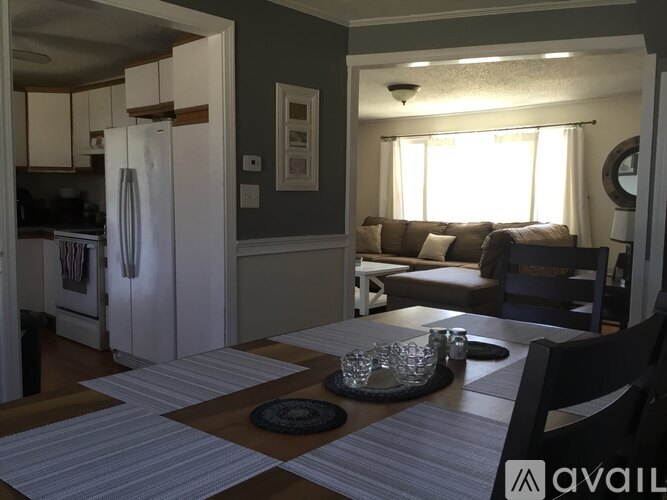 A kitchen with a refrigerator, a dining table with chairs, and a couch in the living room.