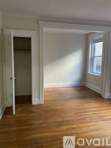 A room with wooden floors and white walls, with a door open to another room.