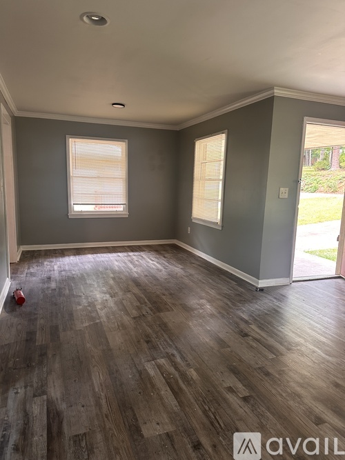 A room with wooden flooring and two windows.