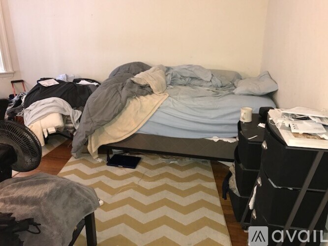 A messy bedroom with a bed, chair, and fan.