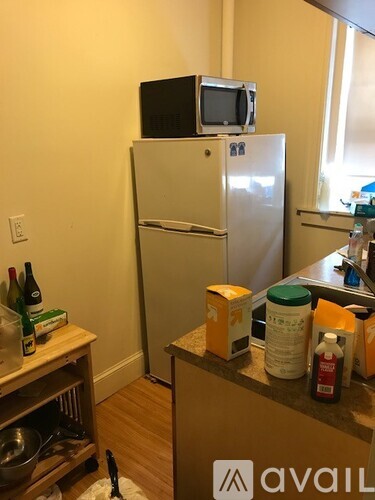 A kitchen with a fridge, a microwave on top of it, and a counter with various items on it.
