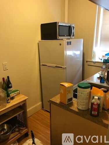 A kitchen with a fridge, a microwave on top of it, and a counter with various items on it.