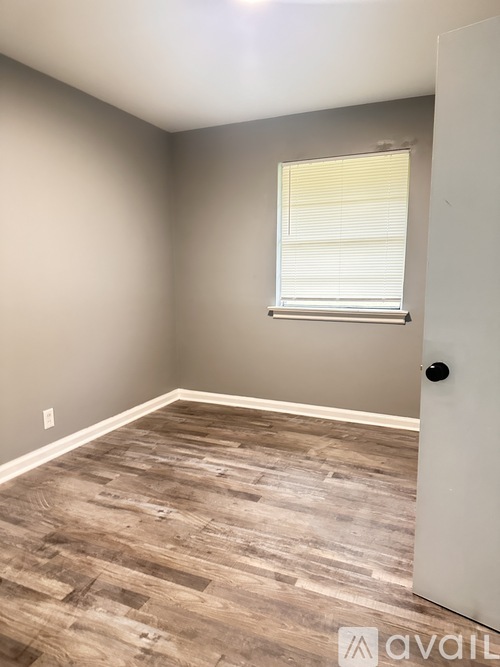 A room with a wooden floor and a window with blinds.