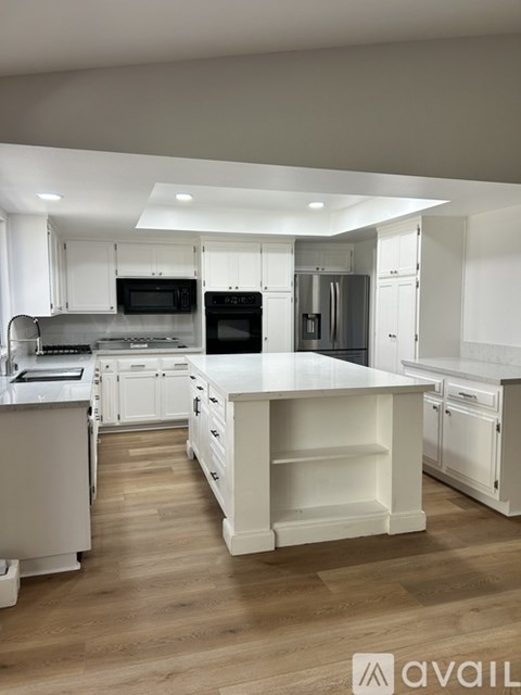 A modern kitchen with white cabinets and a wooden floor.