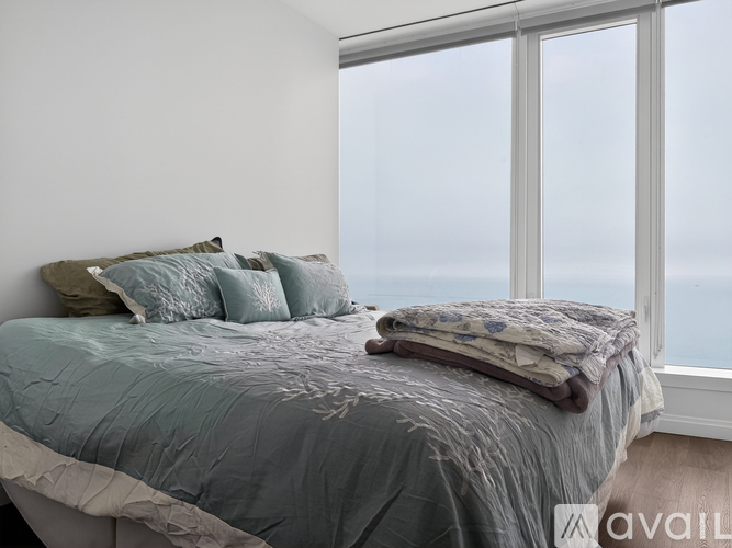 A bed with a grey comforter and a pillow is in front of a window.