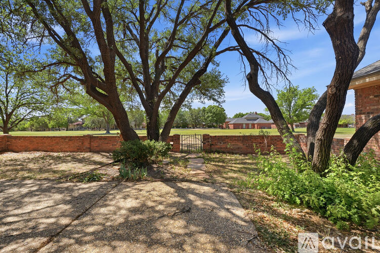 A tree in a yard with a brick wall and a gate.