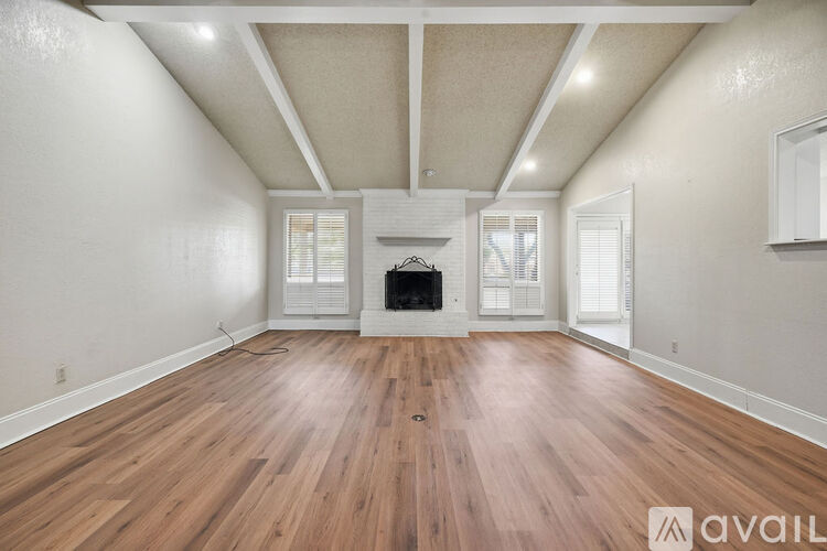 A spacious room with wooden flooring and a fireplace.