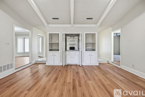 A spacious room with wooden floors and white walls, featuring a kitchenette with white cabinets and appliances.