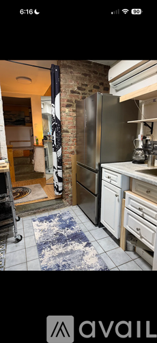 A kitchen with a refrigerator, sink, and a blue rug on the floor.